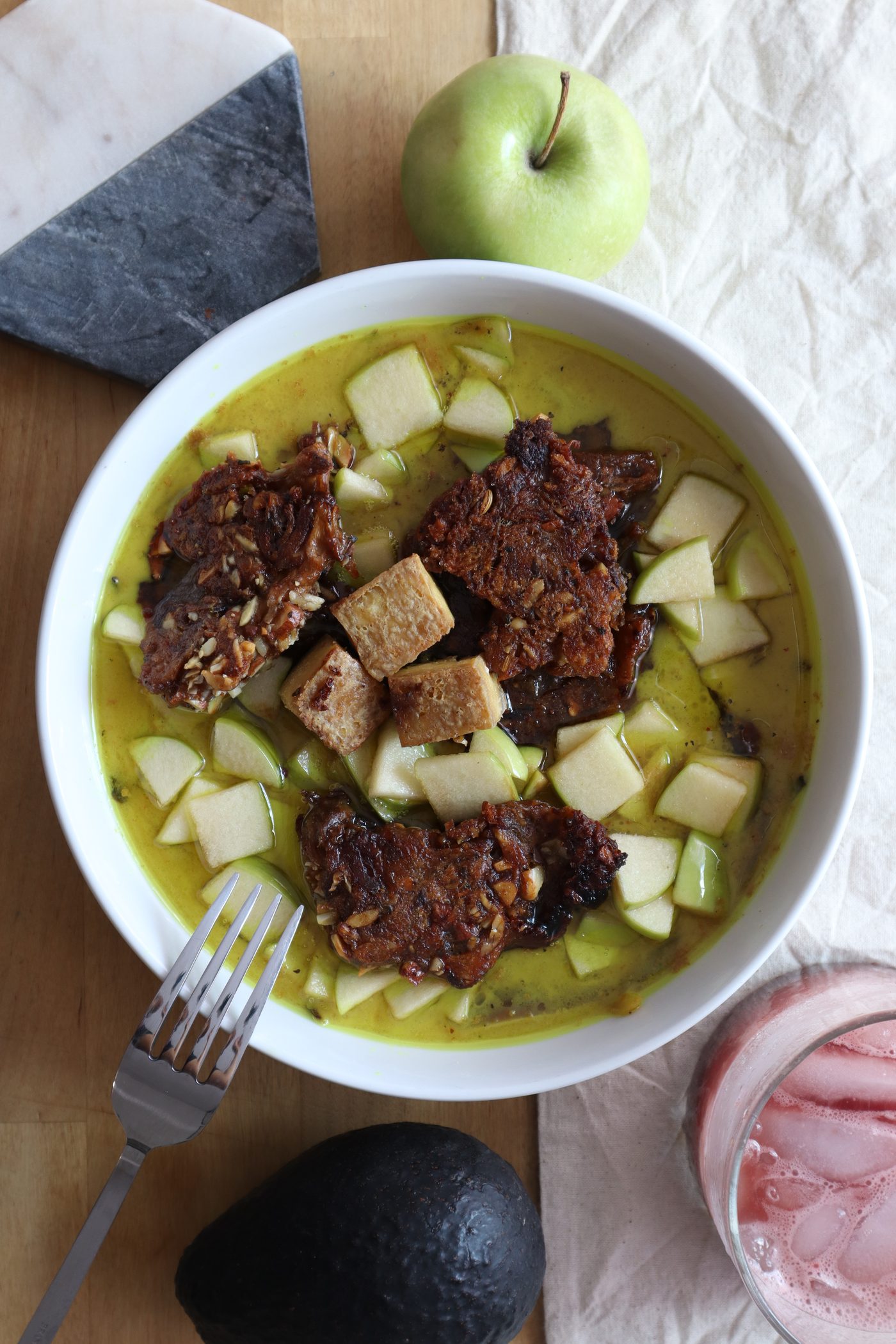 Overhead bowl of golden broth with crispy tofu, sun-dried tomato, apple, and avocado